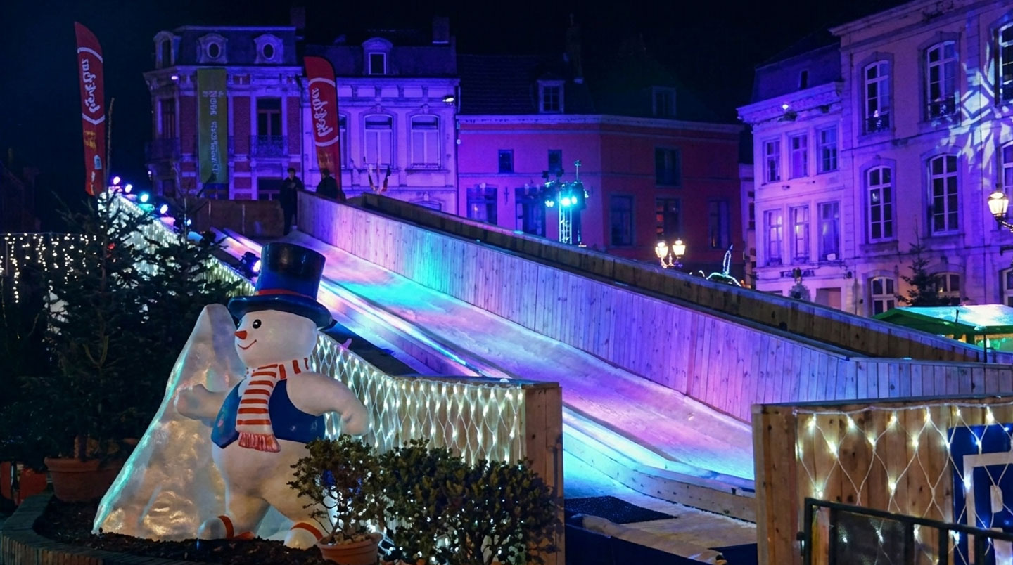 Événement corporate hivernal en cours avec iceberg en résine servant d'îlot conversation au premier plan, guirlandes lumineuses guinguette créant ambiance chaleureuse en second plan, et piste de luge synthétique avec participants enthousiastes en arrière-plan, illustrant les trois leviers immersifs simultanés
